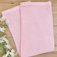 Pink textured blanket on a wooden surface with white flowers.
