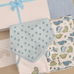 A baby gift set featuring a light blue patterned bib, a white blanket with a blue and green dinosaur print, a textured blue knit swaddle, and a white gift box with a light blue ribbon.